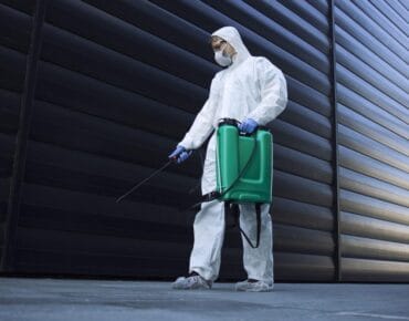 Person in white chemical protection suit doing disinfection of public areas to stop spreading highly contagious corona virus.