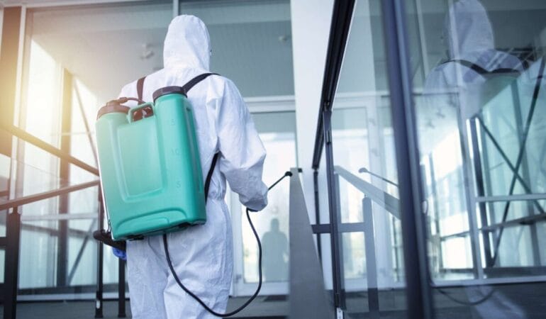 Man with tank reservoir on his back spraying disinfectant to stop corona virus.